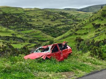 Wrecked red car in a scenic green hillside landscape, highlighting accident damage against a natural background.