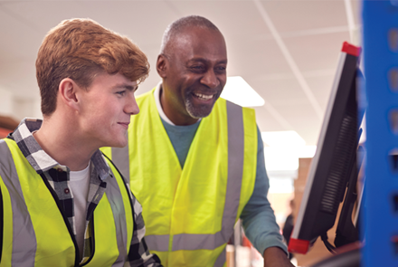 male intern with supervisor working in busy modern warehouse on computer terminal