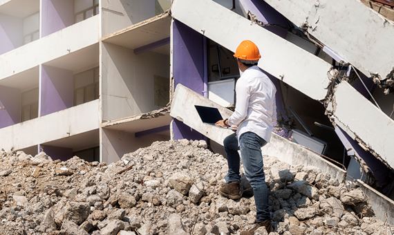 Engineer holding laptop is checking for destruction, demolishing building